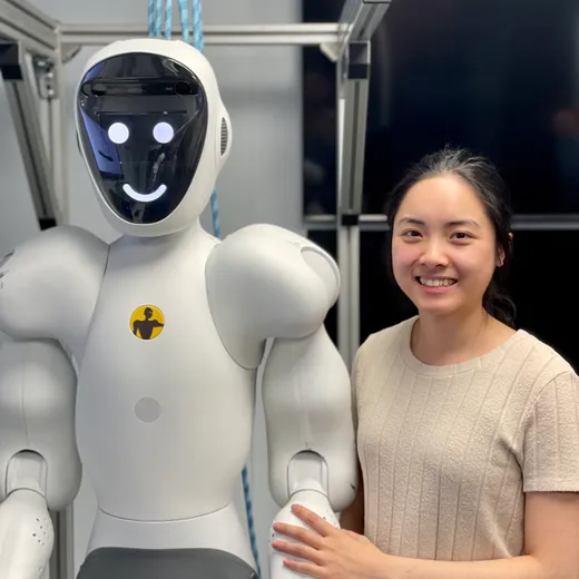 A perception engineer in a lab coat stands beside a white-and-black humanoid collaborative robot in a research lab, adjusting its arm at a workstation.