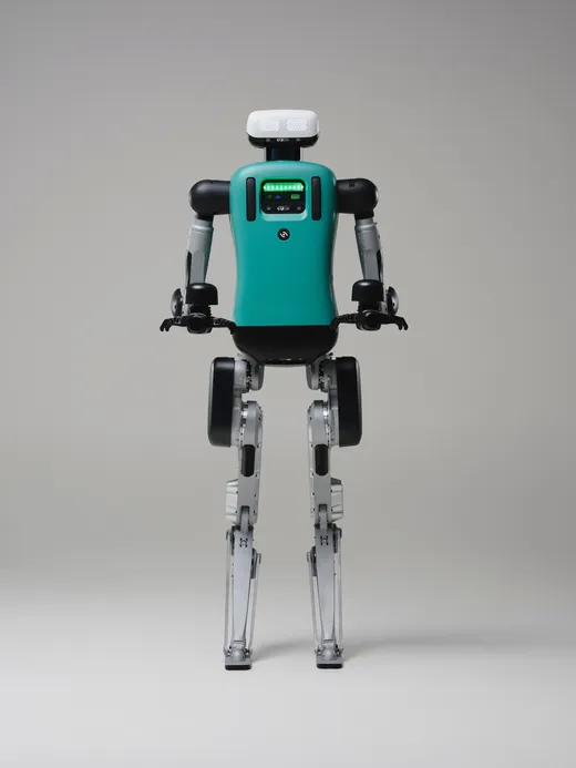 A full-body studio product photograph of Agility Robotics' Digit humanoid robot against a plain gray backdrop, showing its teal torso, white head unit with a dotted LED display, black-and-silver articulated arms with three-fingered grippers, and digitigrade silver-and-black legs.