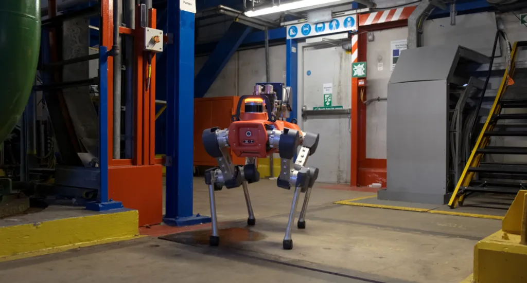 An orange-and-black ANYmal quadruped robot walking through an industrial facility corridor past blue structural beams, safety signage and a grey electrical cabinet.