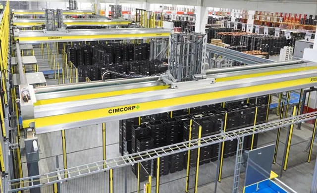 An overhead view inside a distribution center showing multiple parallel yellow, CIMCORP-branded overhead gantry rail robots picking black plastic tote crates above rows of warehouse racking.