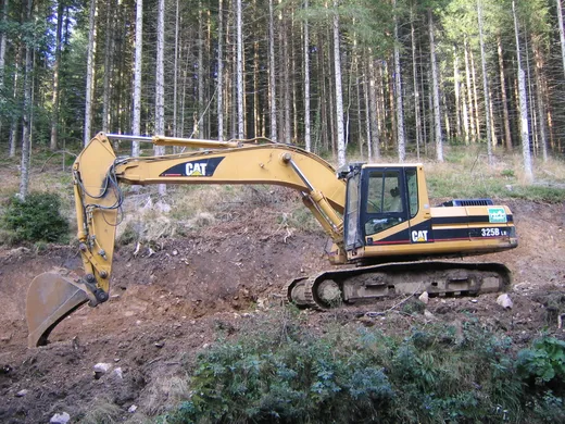 A tracked excavator digging into an earthen embankment.