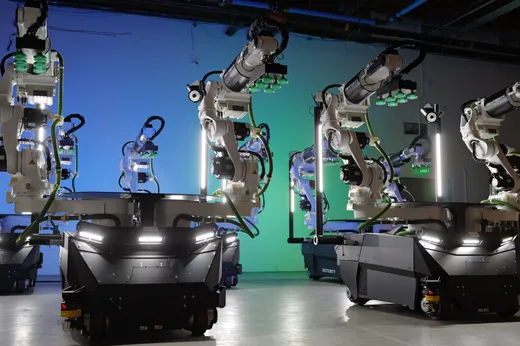 A row of white Kawasaki robot arms, each labeled Dexterity and fitted with green multi-cup suction grippers, mounted on dark wheeled mobile bases in a studio with blue-to-green gradient lighting; a Dexterity-branded cart sits in the background.