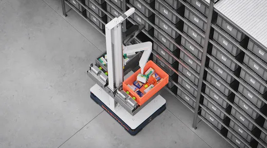 An angled overhead view of a Brightpick Autopicker mobile robot with an articulated arm placing a package into an orange tote, positioned in front of rows of shelved storage bins in a warehouse.