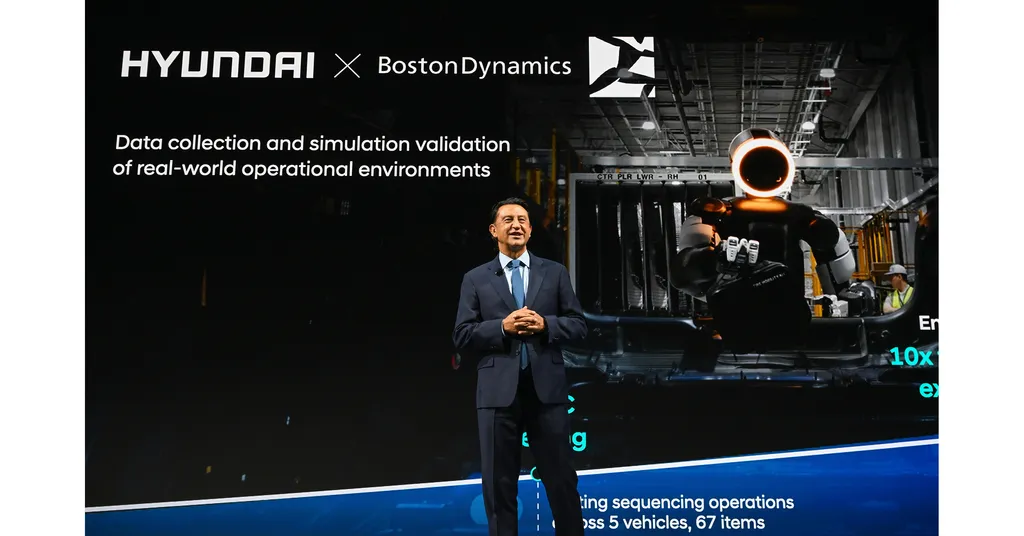 Hyundai Motor Company president and CEO Jose Munoz speaks on stage at an investor-day presentation in front of a large screen reading Hyundai x Boston Dynamics, showing an on-screen photo of a humanoid robot doing parts-sequencing work on a factory floor.